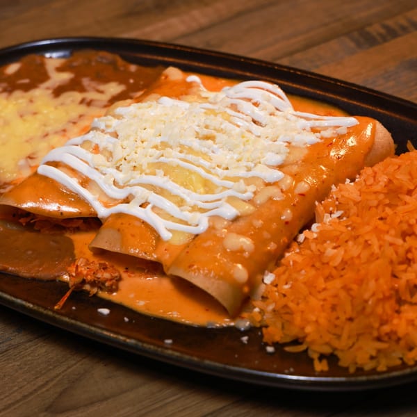 Three enchiladas covered in red sauce, sour cream, and cheese, with a side of red rice.